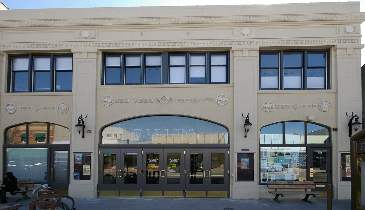The cream-colored facade of the Rialto Theater on 4th Street, with RIALTO lettered in the tall arched window over its row of glass entrance doors and the street number 228 on the side door, under a clear winter sky.