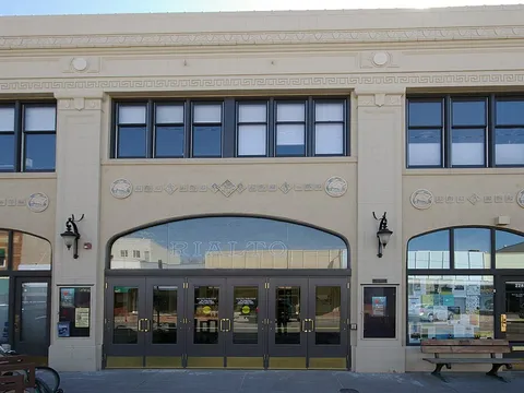 The cream-colored facade of the Rialto Theater on 4th Street, with RIALTO lettered in the tall arched window over its row of glass entrance doors and the street number 228 on the side door, under a clear winter sky.